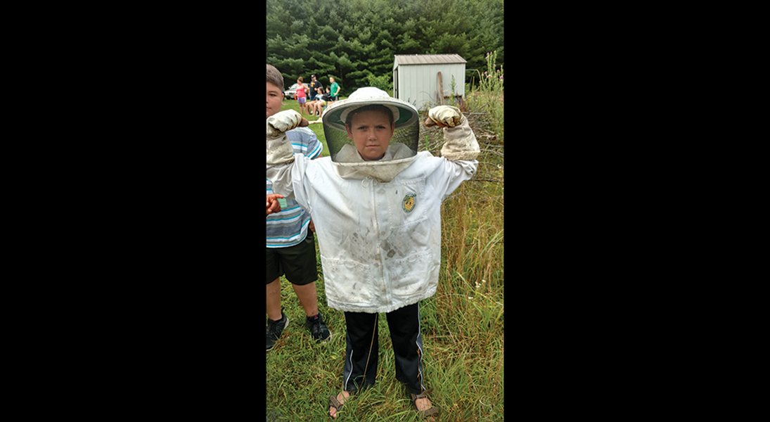 A boy poses in a beekeeper's suit.