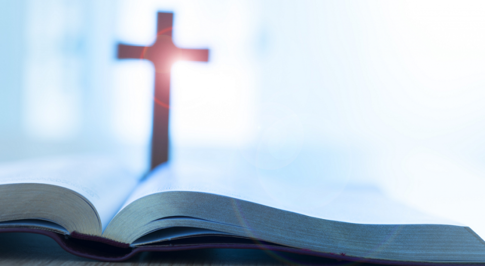 A cross is behind an open Bible.