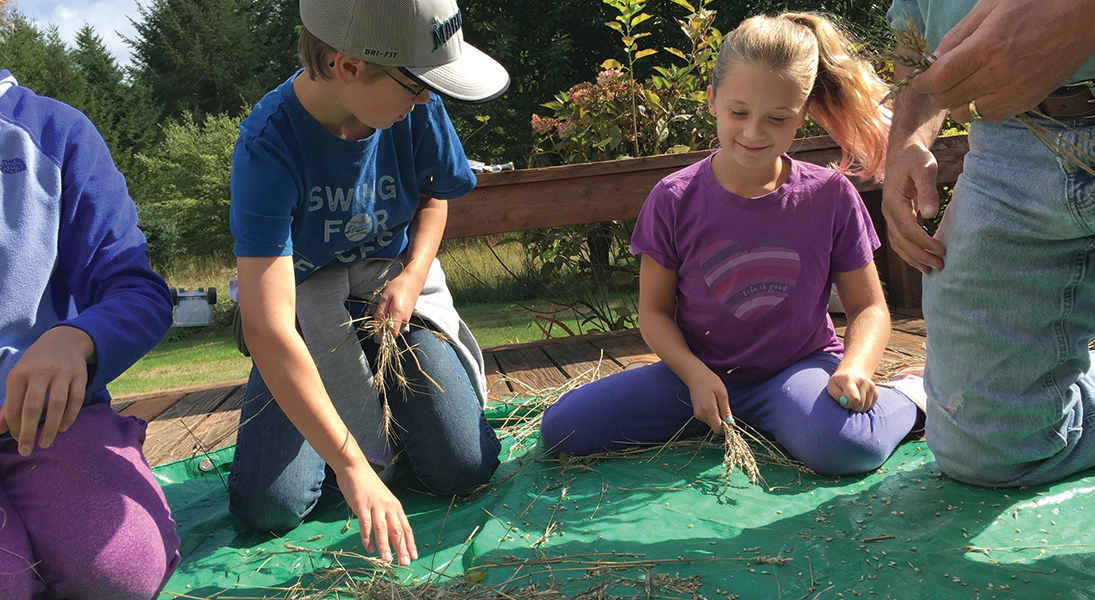 Two children separate wheat from the chaff on a tarp.