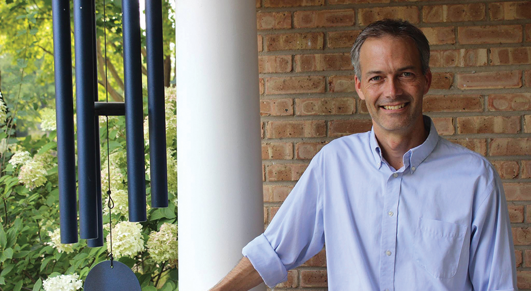Composes James Stephenson poses for the camera before a white pillar and a brick wall.