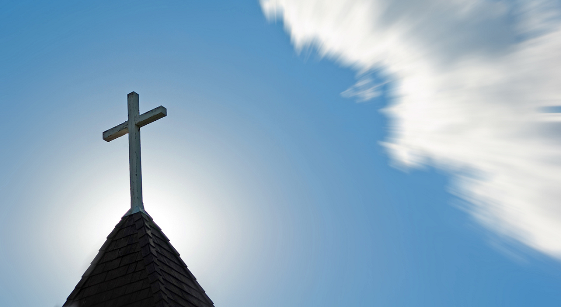 A solitary cross atop a church against a blue sky.