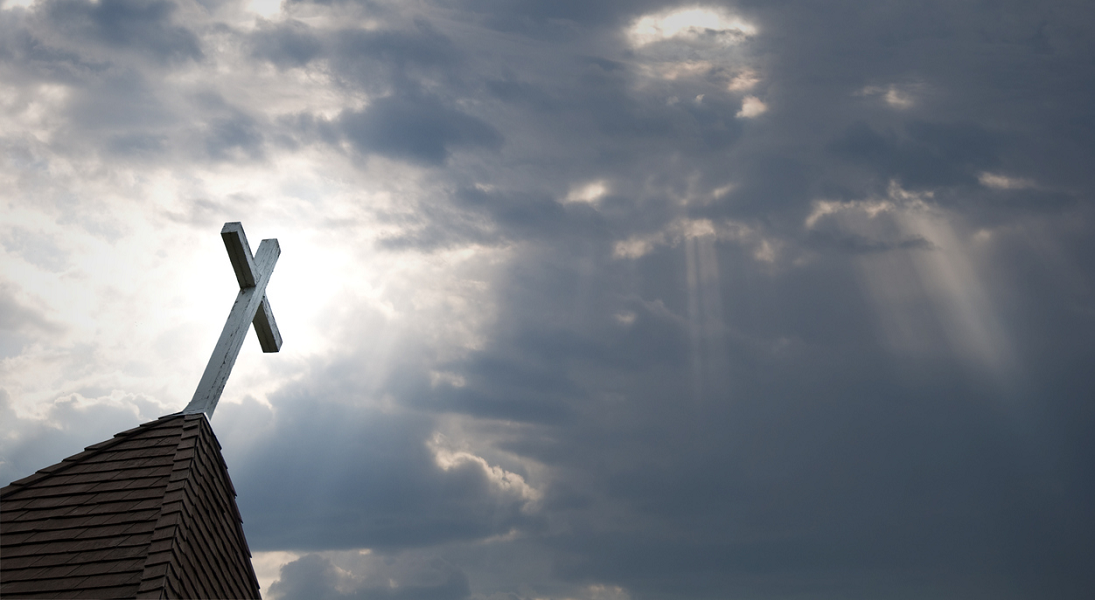 A solitary cross atop a church against a dark, cludy sky.