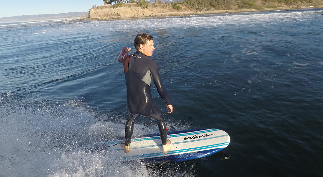 A man in a wetsuit surfs standing on a surfboard.