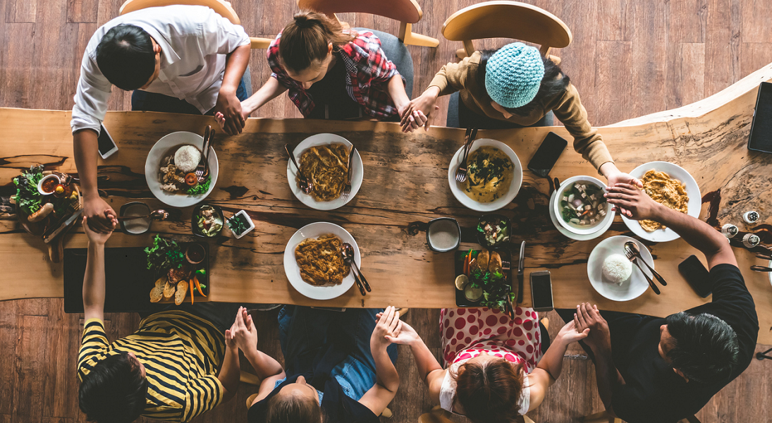 A group of people seen from above hold hands around a table.