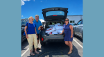 Three people gathered around an open car hatch filled with pillows and bedding